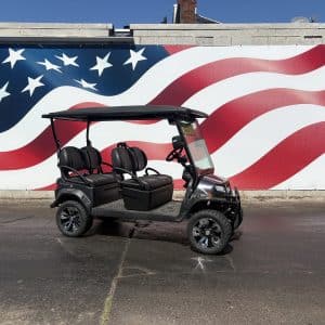 Black golf cart with four seats parked on a paved lot in front of a large american flag mural.