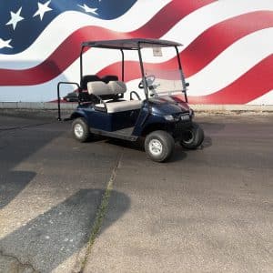 Blue golf cart with beige seats parked on cracked pavement in front of a large American flag mural.