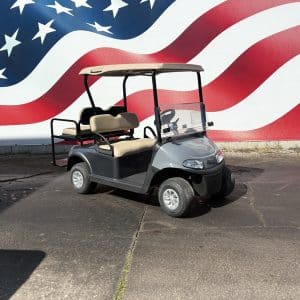 Gray golf cart with beige seats parked in front of a large mural of the American flag with stars and stripes.