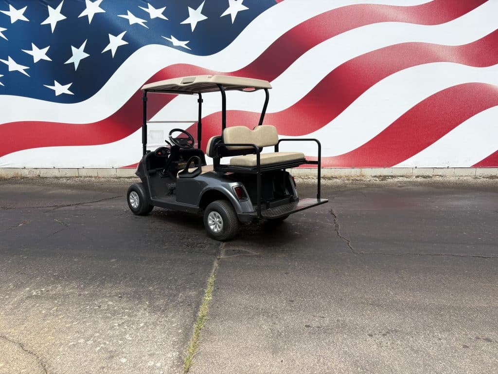 Golf cart with beige seats and roof parked on asphalt in front of a large mural of the American flag.