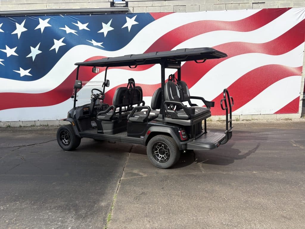 Black golf cart with two rows of seats parked on a street in front of a large american flag mural.
