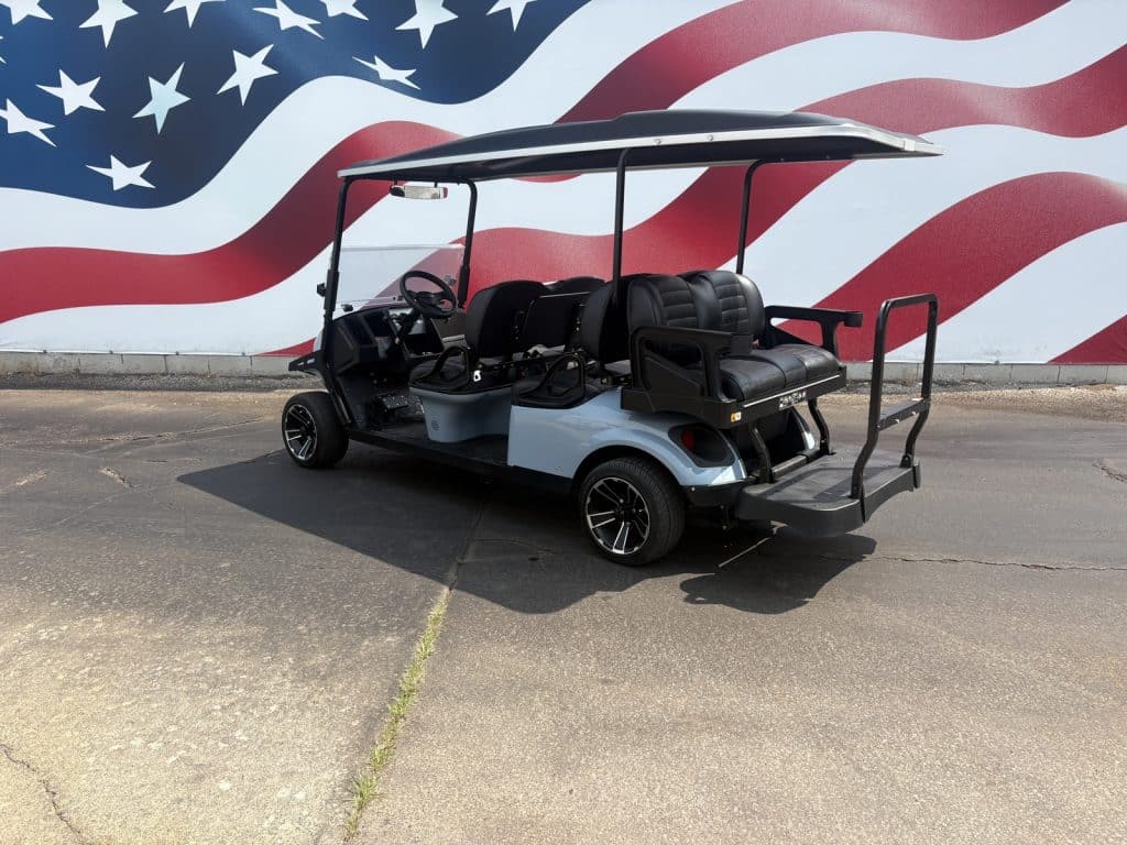 Electric golf cart with four-person seating and a rear platform, parked in front of a large american flag mural on a paved lot