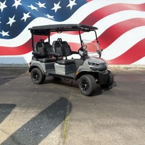 Gray four-seat golf cart with a black canopy parked on a cracked pavement in front of a large american flag mural.