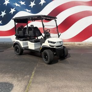 White four-seat golf cart with a black roof parked on a pavement in front of a large american flag mural.