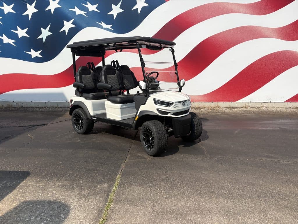 White four-seat golf cart with a black roof parked on a paved lot in front of a large mural of the american flag.