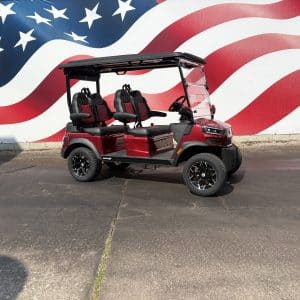 Red golf cart with four seats and a windshield parked in front of a large American flag mural on a wall.