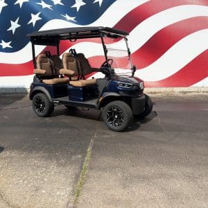 Blue golf cart with tan seats parked on asphalt in front of a large american flag mural behind it.