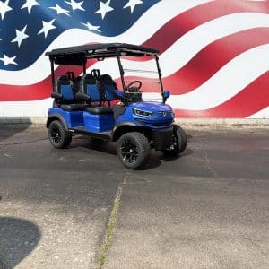 Blue four-seat golf cart with a black roof, parked on pavement in front of a large american flag mural