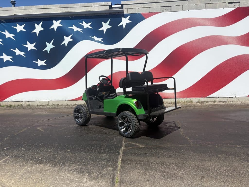 Green golf cart with black roof and seating, parked in front of a large american flag mural.
