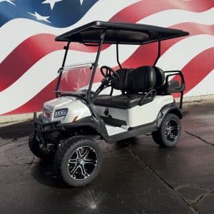 White four-seat golf cart with black roof and seats, parked on pavement in front of a large american flag mural.