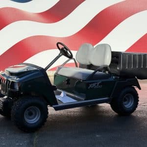Green off-road golf cart with gray bench seats and a large rear cargo box against a red-and-white mural backdrop.