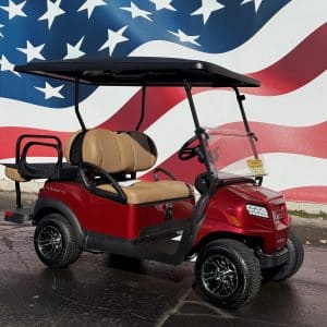 Red golf cart with tan seats and a black roof parked in front of a large U.S. flag mural.
