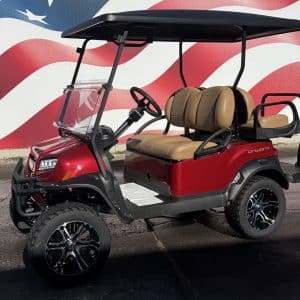 Red golf cart with tan seats and a black roof, parked on pavement in front of a patriotic mural; four-seat configuration with off-road tires.